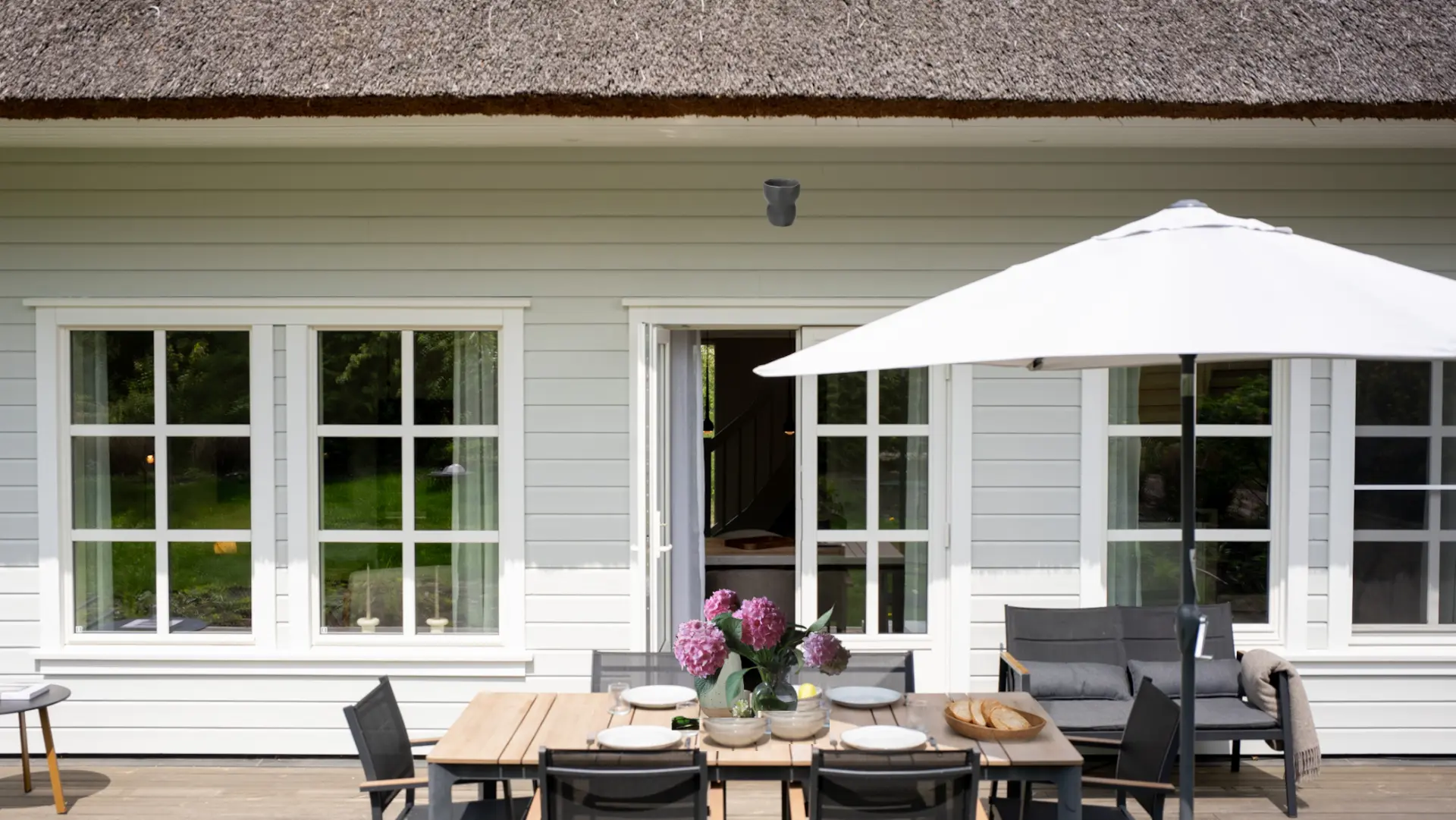 Möblierte Terrasse mit Esstisch, Sonnenschirm und Blick ins Ferienhaus unter Reetdach